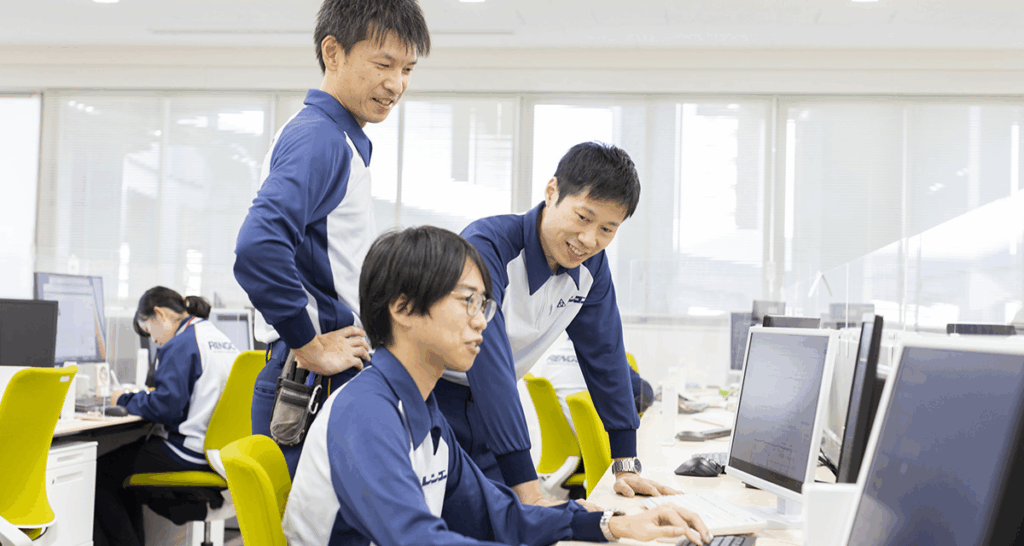 設計をパソコンで行っている男性とそれを見守る男性社員2名